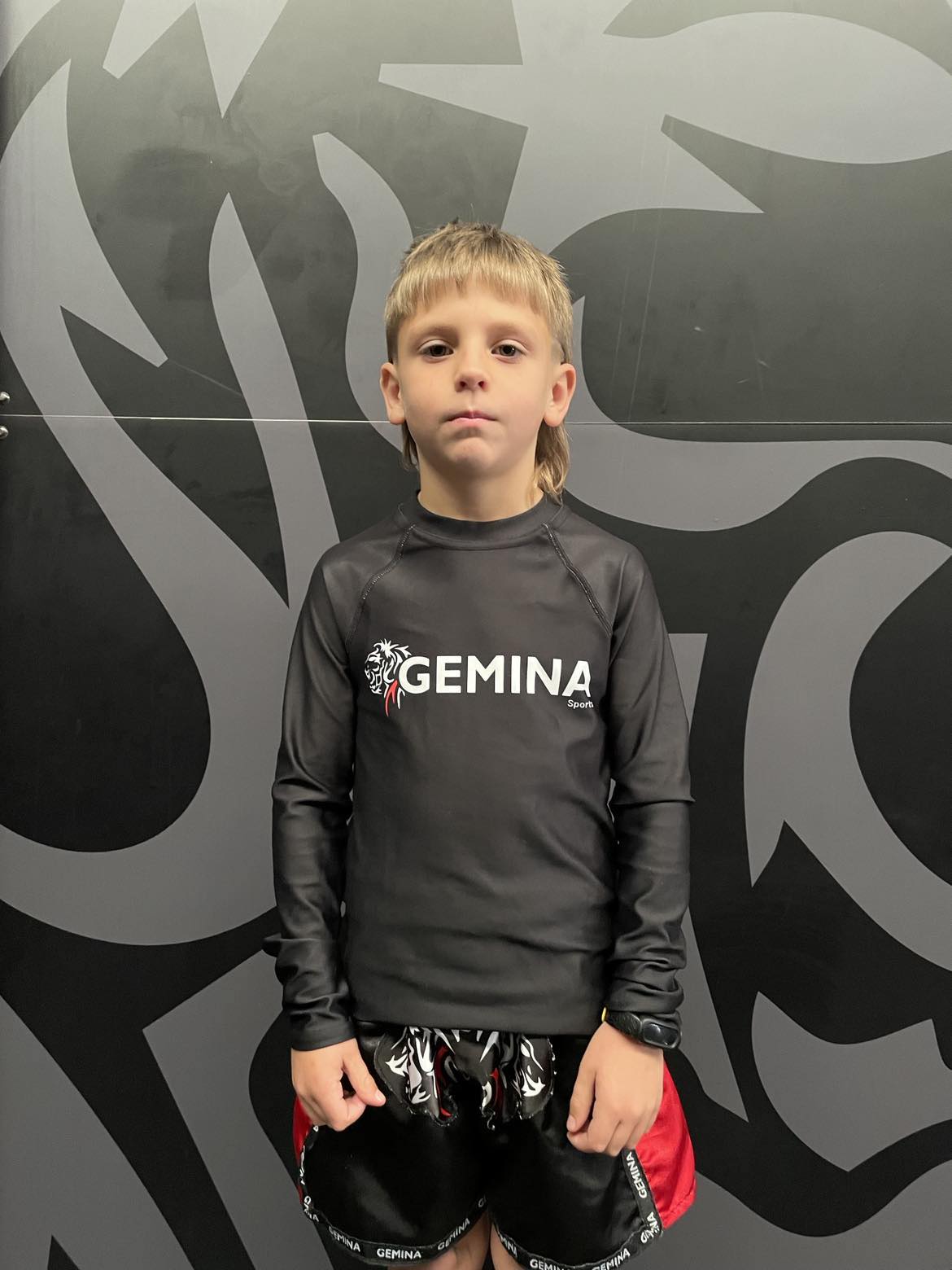 Youth wearing Gemina Youth Rash Guard with brand logo, black color, suitable for water and contact sports.