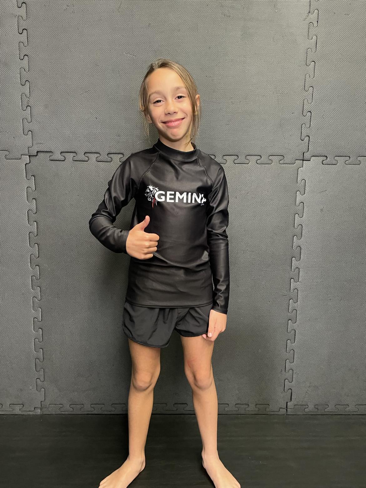 Gemina Youth Rash Guard with UPF 50+, soft four-way stretch fabric, black fitted design, longer body and sleeves for active teens.